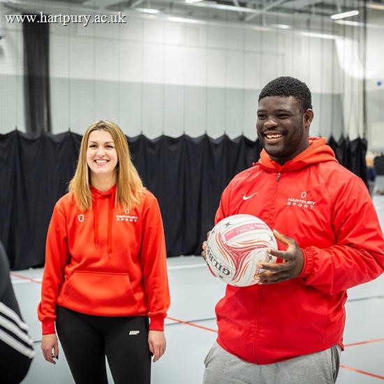 Image of two Hartpury students smiling in a sports hall, with one student holding a football
