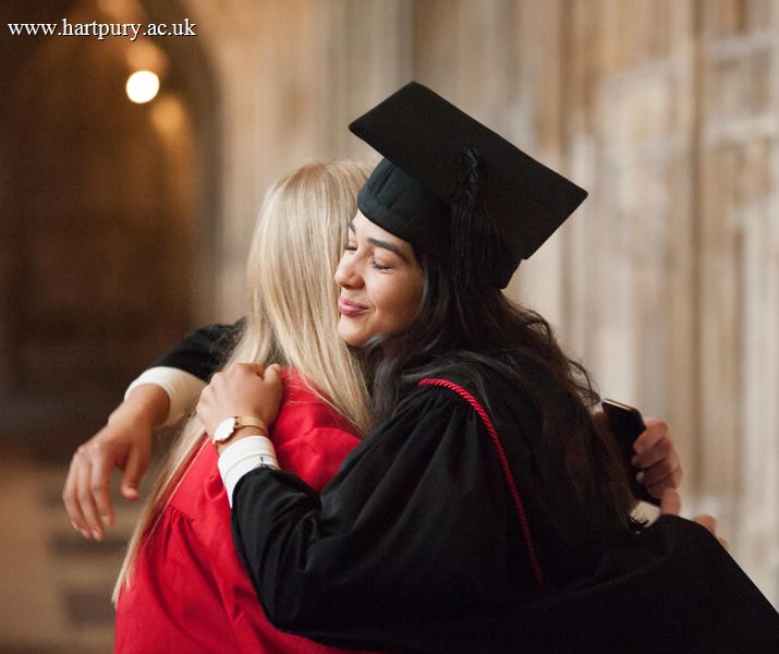 Image of a student smiling in a graduation robe and cap hugging another person