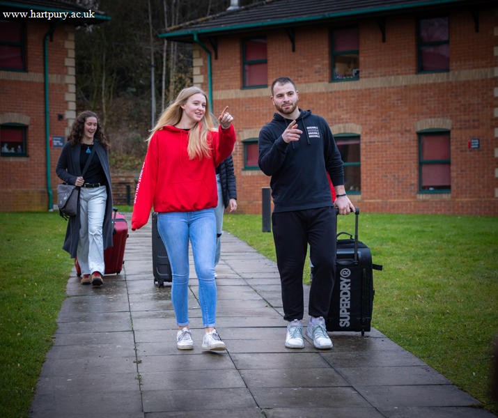 Image of a group of students walking on campus with their luggage on moving in day